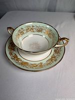 Bowl on underplate showing pattern, handles, gilt trim