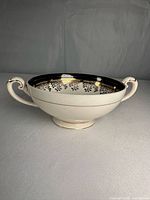 Side view showing twin handles, pedestal foot, navy and gilt interior band