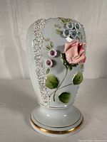 Front view of porcelain vase showing applied rose and floral decoration, gold-trimmed pedestal base