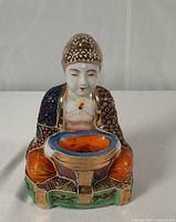 Front view of seated porcelain figure showing bowl and painted details