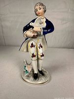 Front view of porcelain gentleman figurine holding dove showing cobalt coat and floral trousers