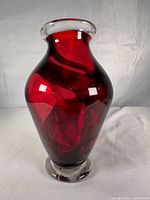 Full view of ruby red glass vase standing upright showing color, shape, clear rim and base