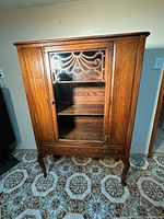 Front view showing carved glass door, interior shelves, drawer, legs