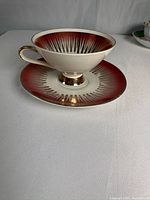Teacup on saucer showing ruby red band, gold sunburst pattern, gold foot and handle
