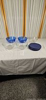 Five glass bowls (two cobalt blue, three clear) and stack of five dark blue lids displayed on table
