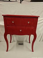 Front view of red lacquer nightstand showing three drawers and cabriole legs