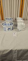 two lidded blue floral soup tureens beside stack of cups