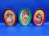 Front view of three oval Coca-Cola tip trays showing graphics and border colors