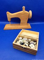 Wooden sewing machine on base beside open wooden box of vintage buttons