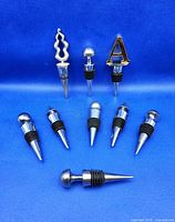 All nine metal wine stoppers arranged on blue backdrop