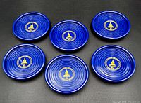 Six cobalt blue coasters showing tops with gold emblem