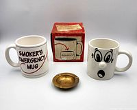 Group shot of brass ashtray, two mugs, and original box
