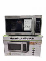 Hamilton Beach stainless steel microwave sitting atop its retail box showing product image and specifications sheet attached to door