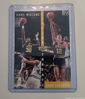 Front of trading card in plastic protective case showing action photos of Karl Malone and John Stockton