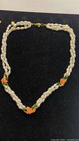 Full view of twisted three-strand pearl-like necklace with green and orange bead accents