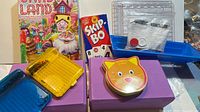 Overview of all games including Candy Land box, Skip-Bo box, cat tin, yellow grid game, blue trays, purple bases