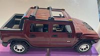 Side view of burgundy die-cast Hummer model showing four doors, truck bed, roof racks