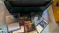 Open green storage box filled with unsorted Magic cards; several loose cards laid in front for reference