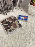 Cigarette case closed beside Blue Jays lighter on rug
