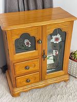 Front view of wood jewellery cabinet showing doors, drawers, stained glass panels, overall shape