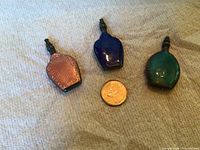 Three enamel miniature perfume dabbers next to coin for scale