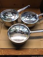 Top view of three Paderno stainless steel saucepans with lids on cardboard