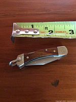 Overall view of closed miniature pocket knife beside measuring tape showing approx 2 in. length