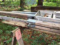 Extension ladder, lumber pieces and sawhorse on forest floor