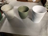 Three ceramic planters (cream with buttons, olive green, white ribbed) displayed side by side