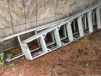 Collapsed aluminum extension ladder with triangular rung supports lying on ground