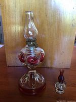 Large pressed-glass oil lamp with red accents and miniature lamp beside it