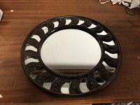 Full view of round cast metal collar mirror on wooden surface