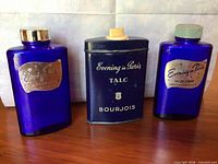Front view of two cobalt blue glass bottles and one navy blue talc tin, all marked "Evening in Paris"