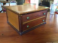 Angled view of custom wooden box showing two drawers, brass knobs, contrasting wood tones, wear on edges