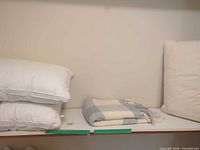 Two stacked bed pillows, folded plaid throw and another upright pillow on shelf