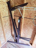 Stacked brown metal bed frame rails leaning against shed wall