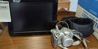 Canon PowerShot camera in front of black digital photo frame with soft case visible