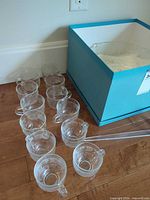 Ten clear glass handled cups alongside blue box