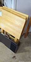 Stack of three light wood folding trays on their stand, darker lap desk leaning in front