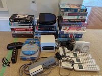 Overview of entire lot including phones, Apple TV box, VHS tapes, power strips, cables, CD case, camera and remote