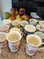 assortment of ceramic mugs with bowl of artificial fruit