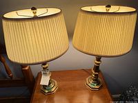 Pair of brass table lamps on wooden surface with shades lit