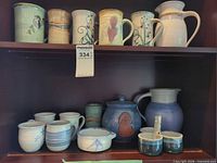 Cabinet shelf showing entire collection of mugs, pitchers, and jar