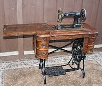 Full view of sewing machine mounted in oak treadle cabinet showing drawers, iron base and extended work surface