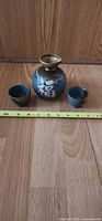 Front view of ceramic sake flask with kanji and two cups beside a measuring tape