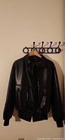 Full front view of black faux leather bomber jacket on hanger