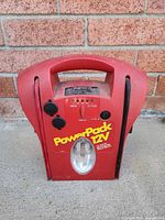 Front view of red PowerPack 12V jump starter showing spotlight lens and branding