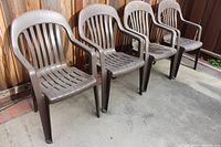 Four brown plastic patio chairs aligned side by side against a wooden fence