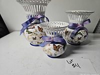 Three graduated porcelain butterfly vases with purple ribbons