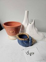 Group shot of four ceramic items: terracotta footed planter, blue shell vase, two white sculptural vases